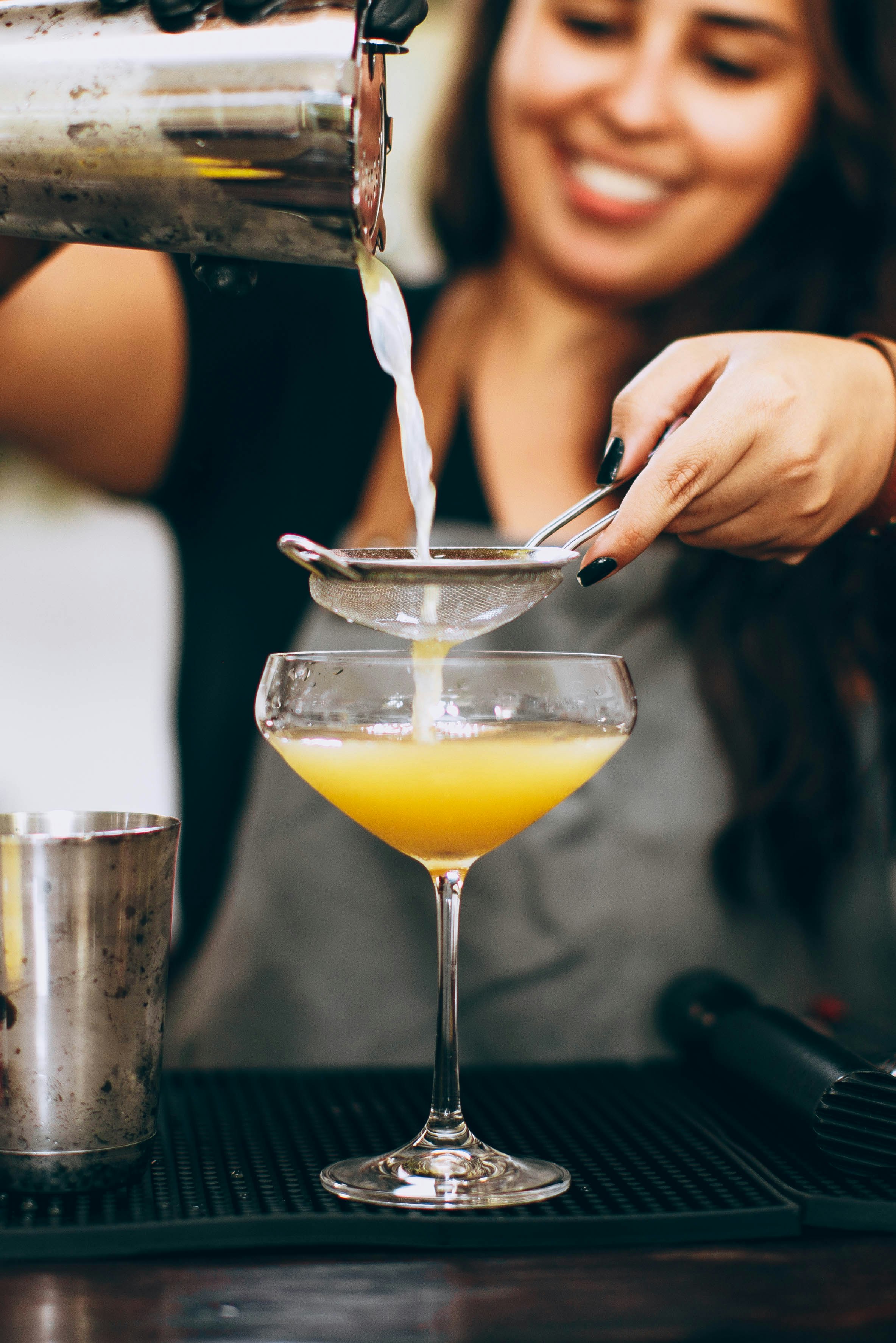 person pouring yellow liquid on clear cocktail glass